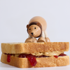 Small teddy bear sitting on a slice of bread with jelly, on a light gray background